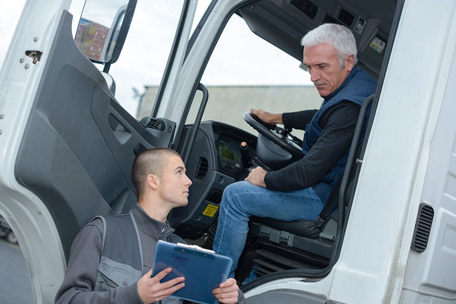 Business Insurance - Senior Truck Driver Sitting in White Truck and Talking to Logistics Manager About the Upcoming Trip